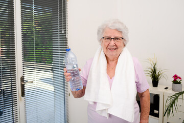 portrait of an active and dynamic senior woman doing sport fitness at home and holding mineral water bottle