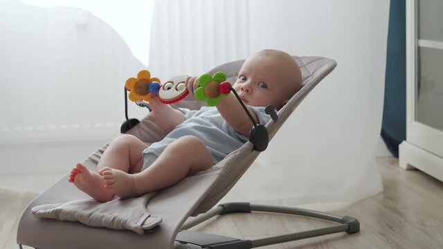 Cute 3 month old baby boy playing with toys in bouncer for kids, infant activity, child playing with wooden toys in rocking chair. High quality 4k footage