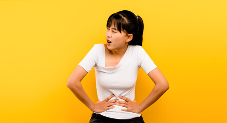 Asian woman with severe stomach ache alone on a yellow background concept of illness and health care - obrazy, fototapety, plakaty