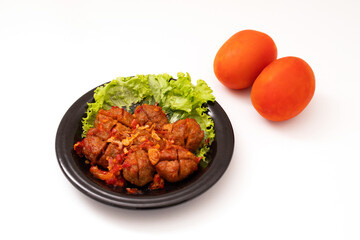 Homemade meatballs with tomato sauce and spices served on a black plate on a white background