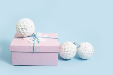 Pink Christmas gift box with white baubles on baby blue. Merry Christmas or Happy New Year greeting card with copy space with snow bokeh lights