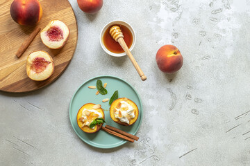 Baked peaches with cinnamon, almond petals, cream cheese, and honey on a light concrete background. Fruits in a plate with mint, top view, copy space.