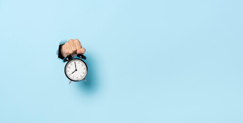 Hand holding black retro alarm clock with text space on blue background.