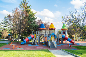 Children playground in public park at sunny day. Colorful swings, seesaw and slides.