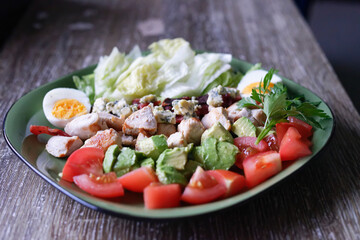 A colourful cobb salad freshly prepared on a green plate