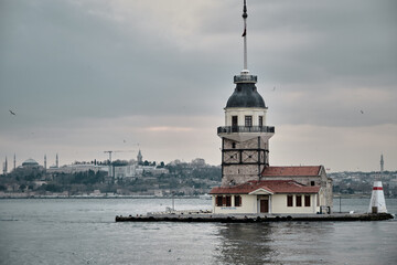 Fototapeta premium The maiden's tower (kiz kulesi) in stanbul, Turkey during overcast weather with sunshine reflection in bosporus sea. Groups of seagulls flying on sea. stanbul Turkey 01.03.2021
