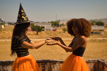 Young Hispanic and Latina women doing hand clapping games and dressed up for Halloween outdoors.