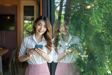 A young woman stands with her smartphone in front of a mirrored glass window.