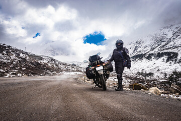 Obraz premium girl solo ridder in ridding gears with loaded motorcycle at isolated road and snow cap mountains