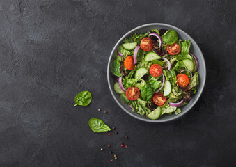 Fresh healthy vegetarian vegetables salad with tomatoes and cucumber, red onion and spinach in grey bowl plate on dark background.