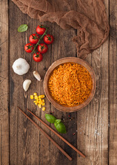 Wooden bowl with boiled red long grain basmati rice with vegetables on wooden table background with sticks and tomatoes with corn,garlic and basil. Top view