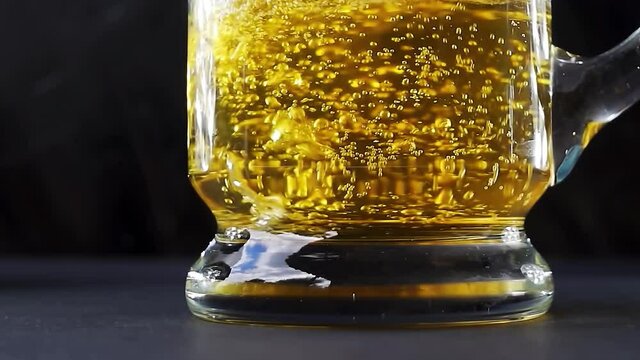 Beer is pouring into a beer mug with bubbles close-up on a black background. 4k slow motion video with the movement of the camera to the right.