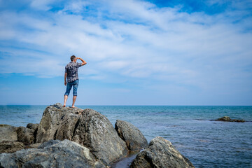 a man on a rocky seashore looks into the distance
