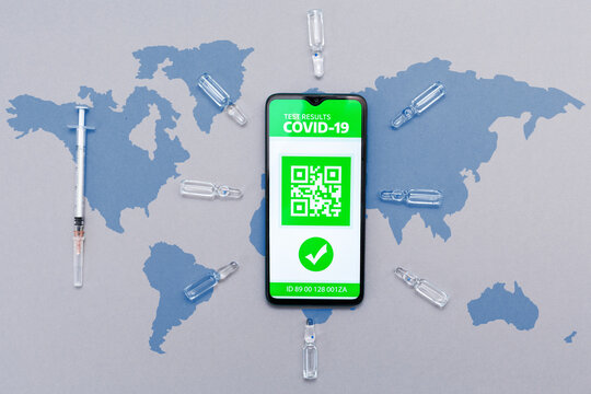 Electronic immunity passport with a COVID-19 vaccination stamp on a smartphone screen with vaccines and syringe. Gray background with a world map. Flat lay. Health and technology concept - Powered by Adobe