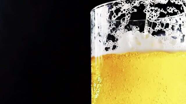 Beer is pouring into a beer mug with bubbles close-up on a black background. Overflowing beer glass with flowing foam. 4k slow motion video 60 fps with the camera moving up.