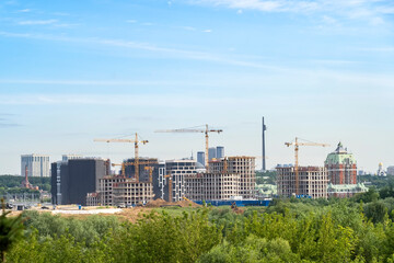 Panoramic view of construction cranes and unfinished residential buildings against clear blue sky. Housing construction, apartment block with scaffolding