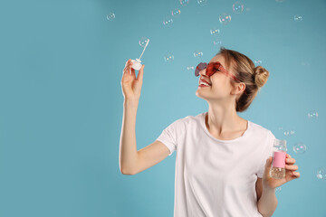 Young woman blowing soap bubbles on light blue background, space for text