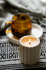 Yellow transparent cup of herbal tea and cozy burning candle on white tray