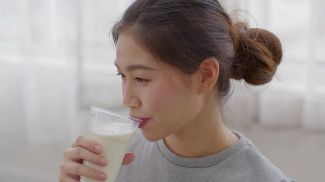 Healthy Young Asian woman Drinking milk with calcium for strong bone at home, Smiling woman holding soy milk on glass enjoy with nutrition wellness life, Wellness with natural milk fresh Concept