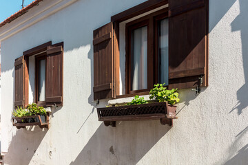 Close up view of traditional, old house with wooden window shutters and flowers in famous Aegean town called 