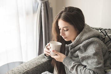 Attractive young woman with cup or coffee sitting  on sofa at home.