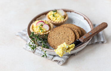 Plate with tartlets, multigrain crackers with egg pate or salad served with radish and thyme.