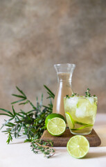 Cold refreshing summer drink or lemonade with lime and thyme on concrete background.