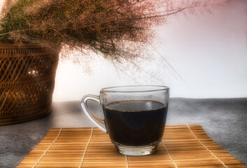 A cup of black coffee on bamboo mat with basket of grass background.