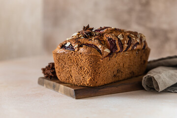 Homemade spicy plum cake decorated with almond on a wooden serving board, concrete background. Loaf cake with plum, spices and almond.