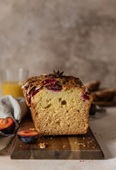 Homemade spicy plum cake decorated with almond on a wooden serving board, concrete background. Loaf cake with plum, spices and almond.