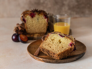 Homemade spicy plum cake decorated with almond on a wooden serving board, concrete background. Loaf cake with plum, spices and almond.