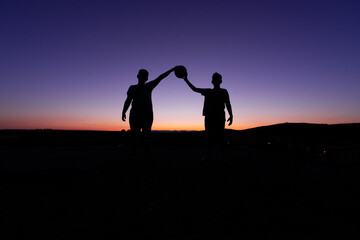 Fototapeta na wymiar SILHOUETTE OF TWO CHILDREN AT SUNSET PLAYING BALL.