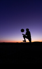 SILHOUETTE OF A BOY PLAYING BALL AT SUNSET