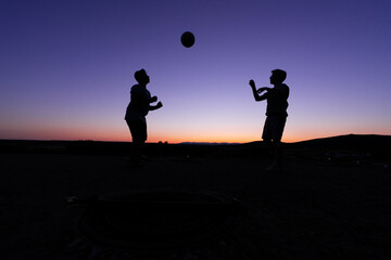 SILHOUETTE OF TWO CHILDREN AT SUNSET PLAYING BALL.