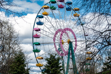 A huge old multi-colored Ferris wheel in a recreation and entertainment park among the branches of...