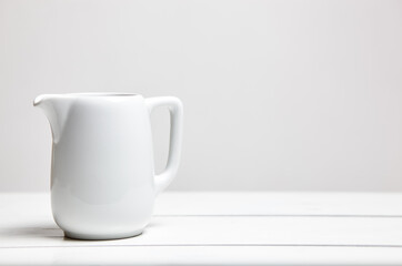 Empty milk jug on wooden background. Porcelain sauce boat, pitcher, creamer or ceramic gravy boat