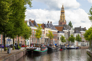 Historic ships, canal houses and warehouses on the old harbor at the Hoge der A with the tower of the historic Der Aa church in Groningen in the background. - obrazy, fototapety, plakaty