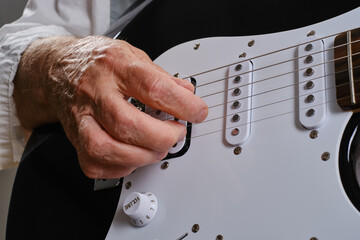 An elderly woman is learning to play the electric guitar. Hands of an elderly man play the guitar. Selective focus