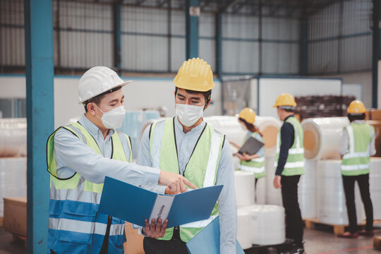 Factory manager and engineer in medical mask and safety protective suite using computer laptop and digital tablet working discuss together