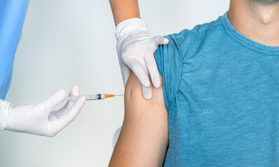 Nurse or medical staff in white gloves putting the vaccine with a needle in the arm to a boy for...