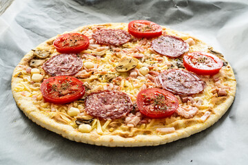 Uncooked circle pepperoni pizza with mozzarella, salami and tomatoes on wooden table
