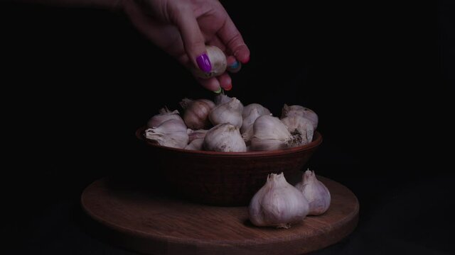Pile of whole bulbs of garlic in ceramic bowl on table. Woman's hand puts the garlic in a plate