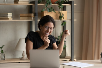 Close up overjoyed businesswoman in glasses celebrating success, yes gesture, using laptop, sitting...