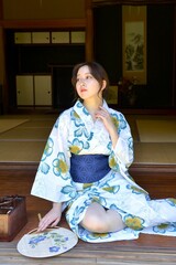 古民家の縁側にたたずむ浴衣姿の若い女性