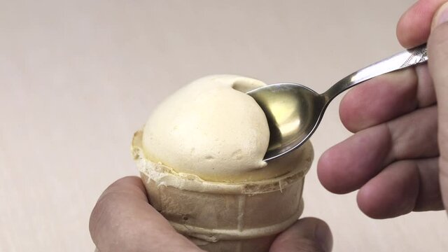 A man with a metal spoon eats ice cream in a waffle cup.