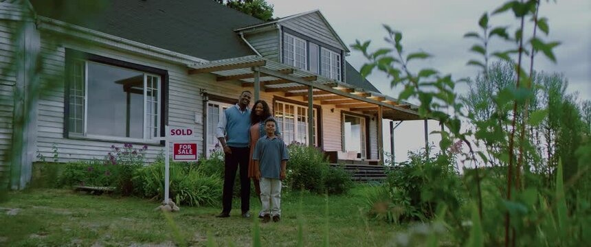 Portrait of happy African American Black family posing near sold sign, their new house in the background. Shot with 2x anamorphic lens
