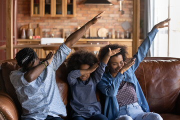 Happy young African American family with small teen daughter dance together do popular viral dab gesture. Overjoyed biracial parents with little teenage ethnic girl child have fun relax at home.