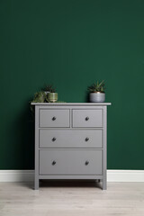 Modern chest of drawers with houseplants near green wall indoors