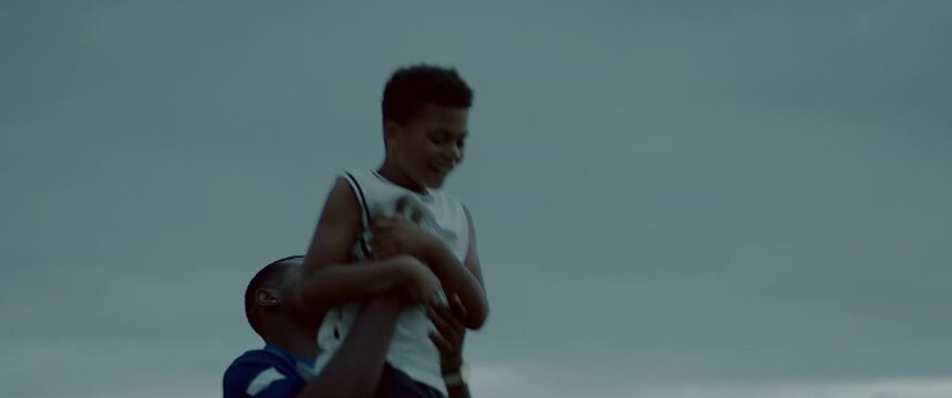 HANDHELD African American father and son playing together on a lawn in front of their house in the evening. Shot with 2x anamorphic lens