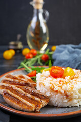 Rice with grilled pork meat, tomatoes and green herbs on dark background